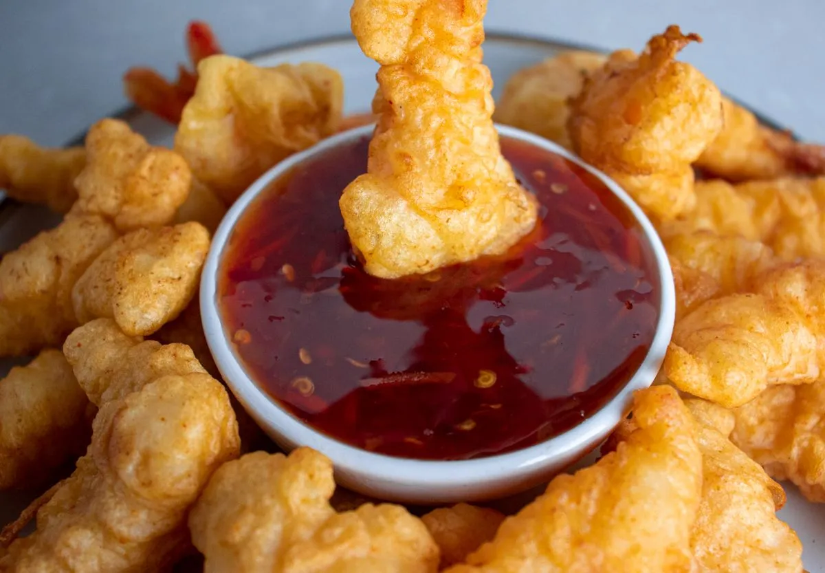 Crispy fantail shrimp being dipped in sweet and sour sauce