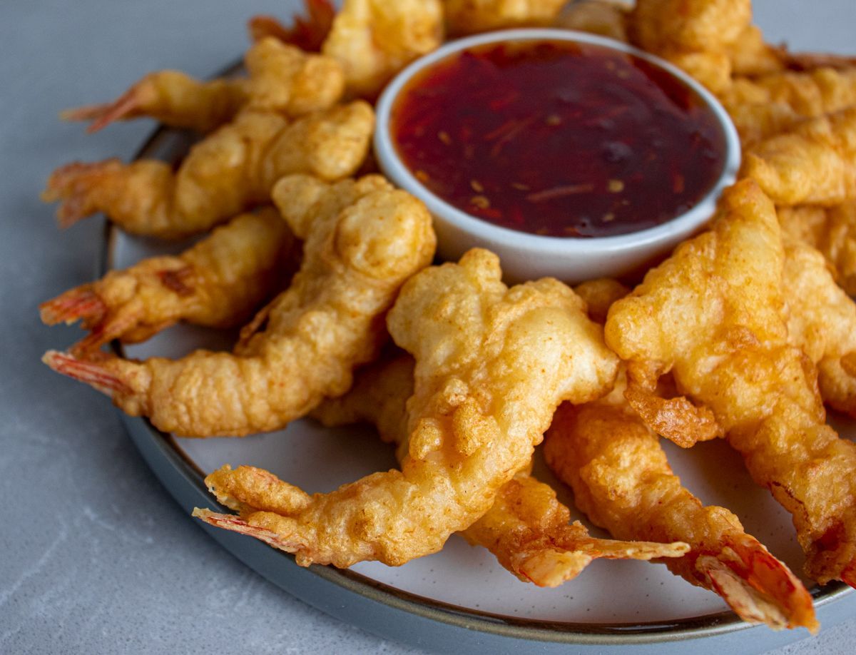 A plate of golden fantail shrimp with tails intact, arranged around a bowl of sweet and sour dipping sauce.